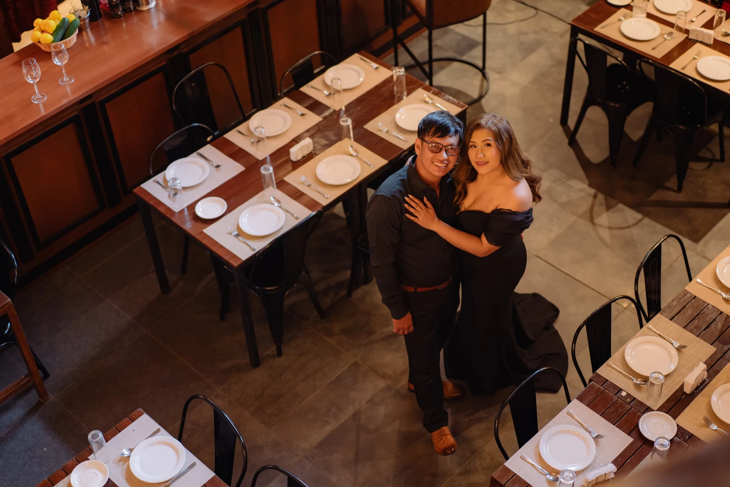 Ryan and Anne embracing beneath the café balcony in a wide overhead portrait.