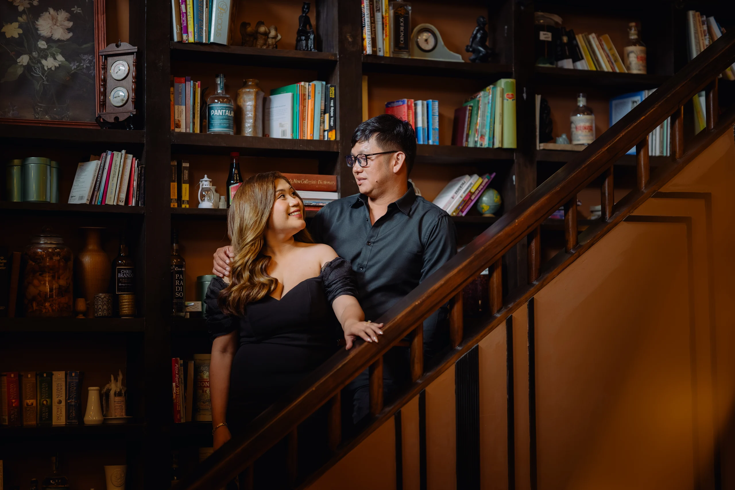 Ryan and Anne embracing on the staircase beside books and lanterns.